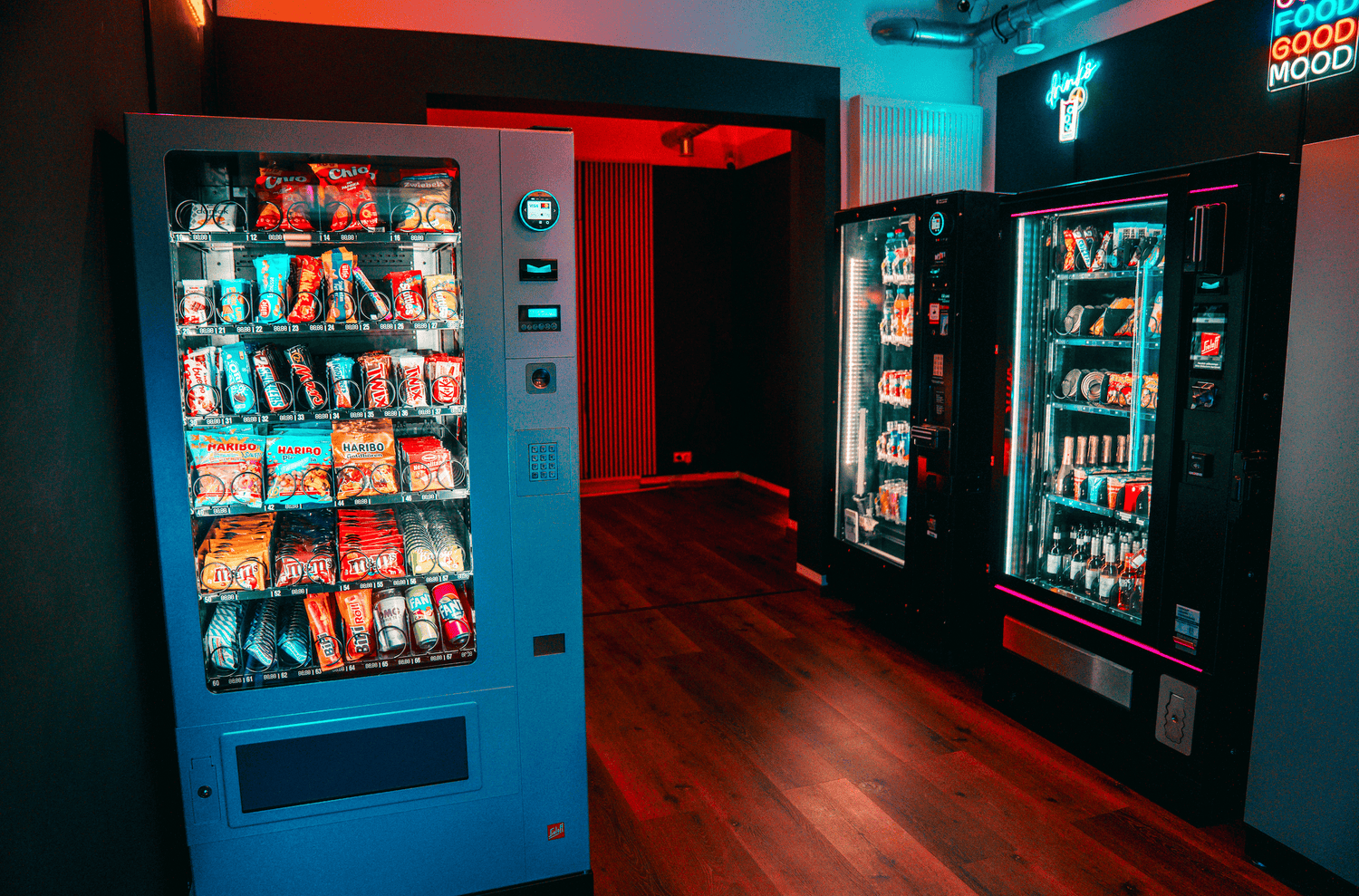 Auf dem Foto ist das innere des Ladenlokals Quickmart 24 in Landau zu sehen und zeigt die verschiedenen Automaten und dessen Sortimente. Die gezeigten Automaten sind von den Herstellern SandenVendo und Sielaff. Neonschilder prägen das Ambiente.